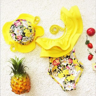 Stylish children`s swimsuit for girls with an interesting ruffle and hat, in yellow with a floral print